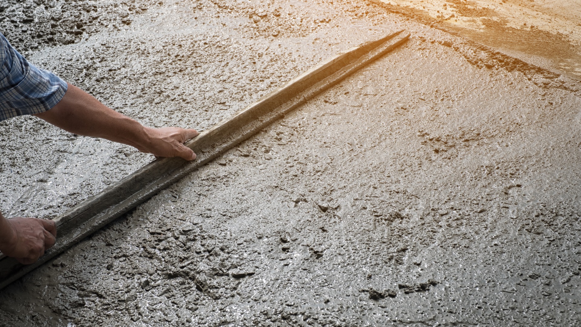 Ein Arbeiter, der keine Arbeitsstiefel trägt und mit einer Hacke (Schaufel) auf einem Betonboden gräbt; Bauarbeiter, die einen Betonbelag ebnen. Ausbau einer Wohnstraße durch das Einebnen einer Betonplatte, Baustelle