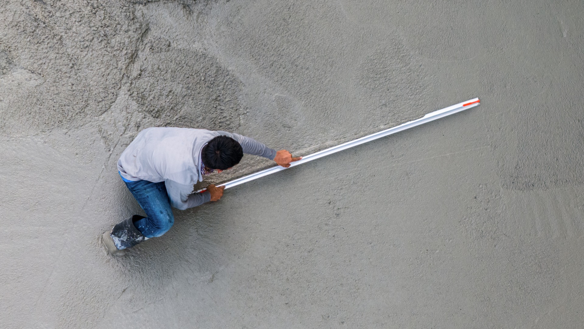 Ein Bauarbeiter glättet nassen Zement mit einer Kelle. Baustelle, Betonarbeiten, Bauindustrie. Luftaufnahme von oben.